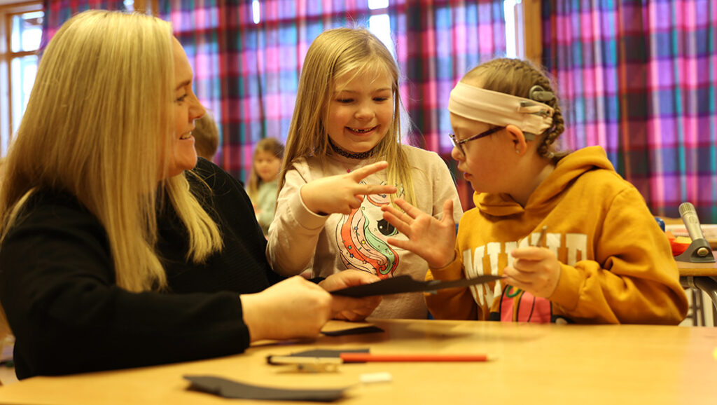 En lærer og to elever ved en pult i et klasserom
