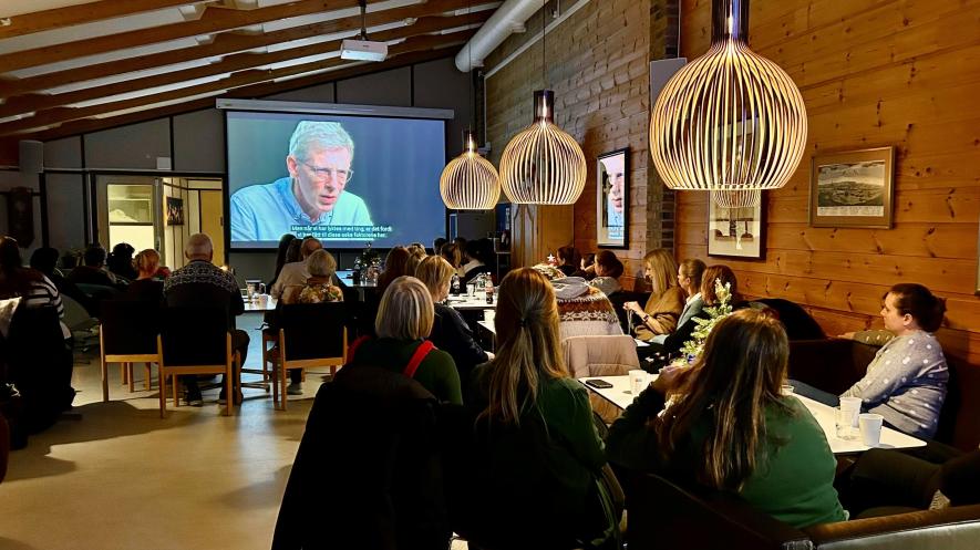 Bildet viser personer som sitter i et rom og ser film på en storskjerm
