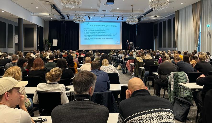 Bilde av personer som sitter i en konferansesal under foredrag