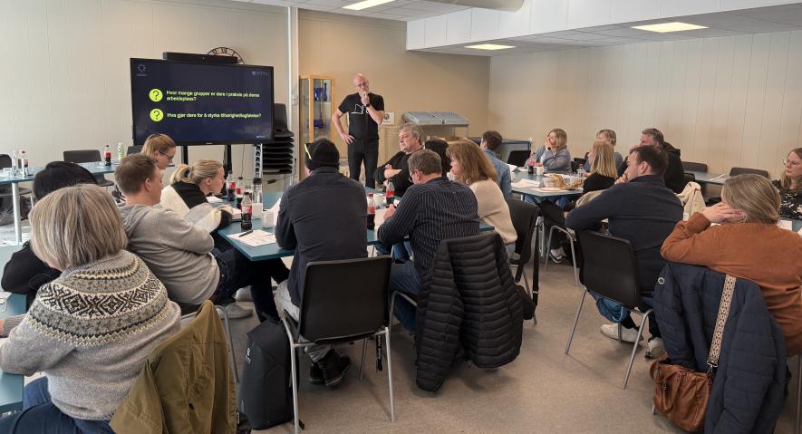 Bildet viser mann som står foran en gruppe sittende mennesker i et rom