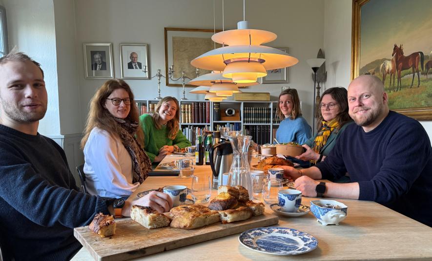 Bildet viser seks personer som sitter rundt et bord og det står mat på bordet.