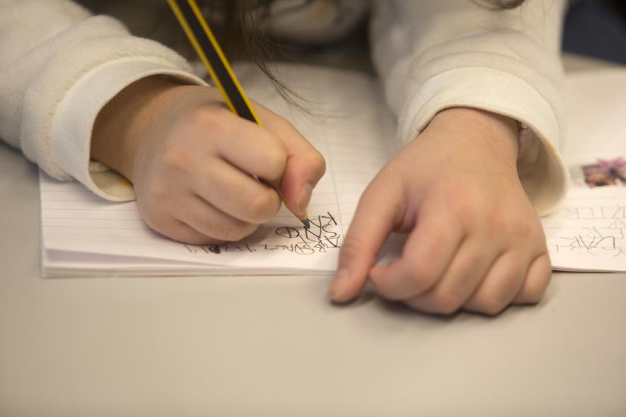 Bilde av to barnehender som holder til en blyant og skriver på et ark
