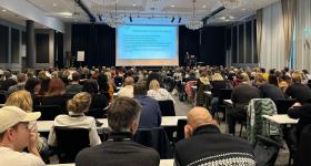 Bilde av personer som sitter i en konferansesal under foredrag